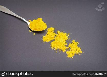 Turmeric or curcuma powder on metal spoon and scattered on dark background.. Turmeric powder on metal spoon