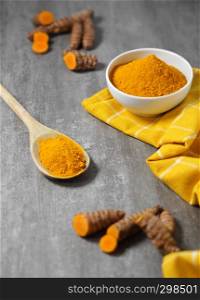 Turmeric powder and roots healthy spice Asian food background with sliced turmeric roots and powder in a white bowl and a wooden spoon.