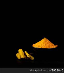 Turmeric powder and roots or barks in black bowl on black background