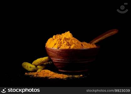 Turmeric powder and roots or sticks in wooden bowl on black background