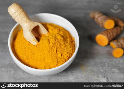 Turmeric powder and sliced turmeric roots healthy spice Asian food closeup of a white bowl with a wooden bailer.