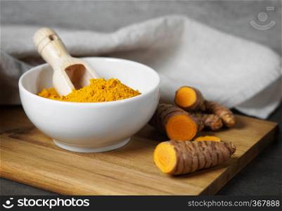 Turmeric powder and sliced turmeric roots healthy spice Asian food closeup of a white bowl with a wooden scoop with copy space.