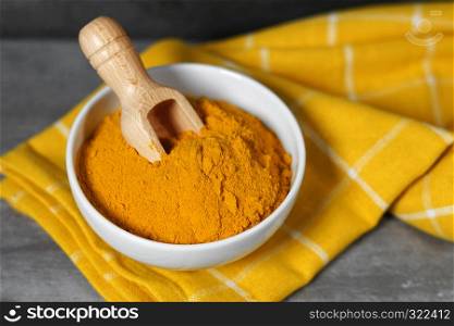 Turmeric powder healthy spice Asian food closeup of a white bowl with a wooden bailer.