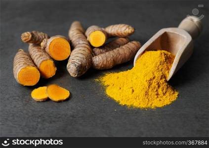 Turmeric powder healthy spice Asian food closeup of turmeric roots sliced and a wooden bailer on a rustic dark grey kitchen board.