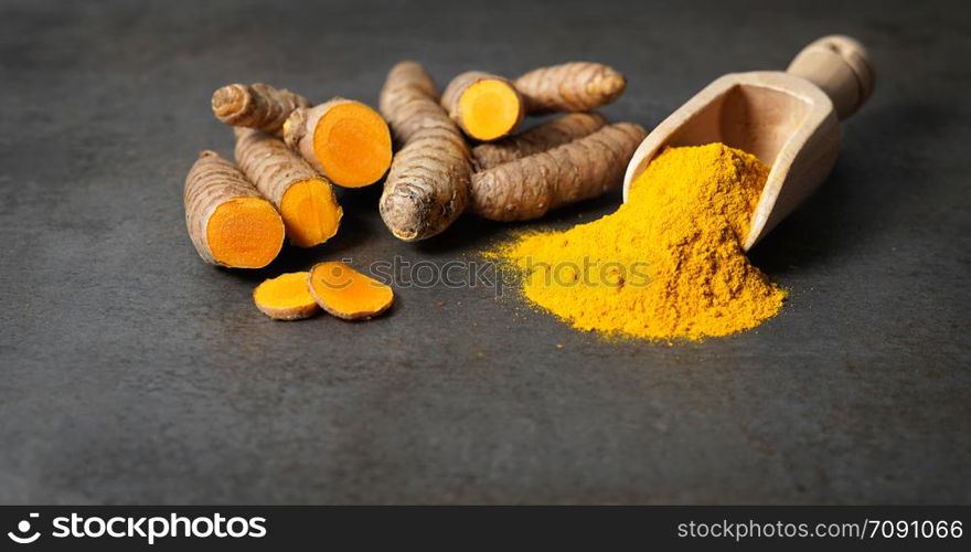 Turmeric powder healthy spice Asian food closeup of turmeric roots sliced and a wooden bailer on a rustic dark grey kitchen board with copy space.