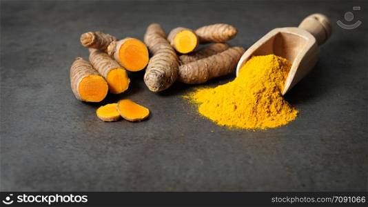 Turmeric powder healthy spice Asian food closeup of turmeric roots sliced and a wooden bailer on a rustic dark grey kitchen board with copy space.