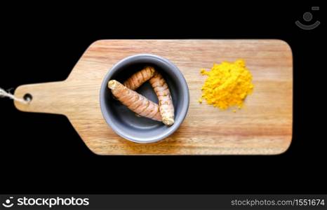 Turmeric root in bowl and spice powder on a wooden cutting board. Isolated on black background. Turmeric root in bowl and spice powder on a cutting board