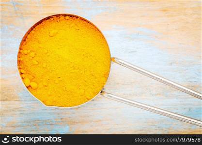 turmeric root powder on a metal measuring scoop over wood background