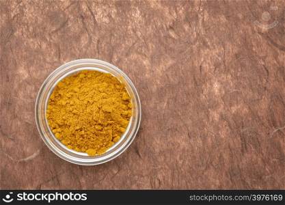 turmeric root powder - top view of a small glass bowl against brown mulberry paper with a copy space