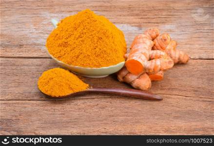 Turmeric roots with turmeric powder on wooden background
