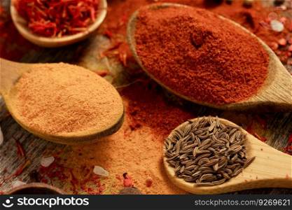 Turmeric spice in spoon and paprika, pepper, turmeric in spoon on table background. Variety of dried spices and seeds ingredients at kitchen table closeup