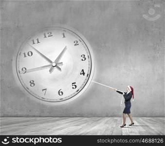 Turn back the time. Woman in Santa hat pulling clock with rope