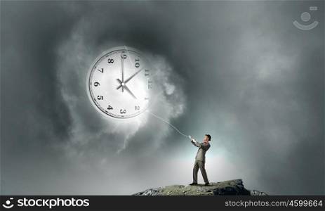 Turn back time. Young businessman trying to turn back time by pulling clock with rope
