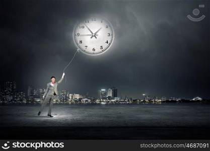 Turn back time. Young businessman trying to turn back time by pulling clock with rope