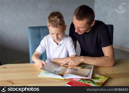 turn the page, look at pictures, read a book, drawings, flip through a page, home leisure, child and parent. boy, dad and son, home schooling, sitting at the table, lots of books. A cute boy is sitting at the table with his dad and watching a book about snakes