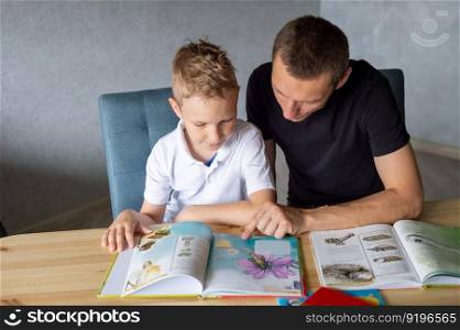 turn the page, look at pictures, read a book, drawings, flip through a page, home leisure, child and parent. boy, dad and son, home schooling, sitting at the table, lots of books. A cute boy is sitting at the table with his dad and watching a book about butterflies