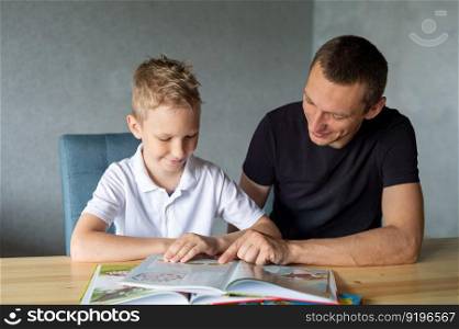 turn the page, look at pictures, read a book, drawings, flip through a page, home leisure, child and parent. boy, dad and son, home schooling, sitting at the table, lots of books. A cute boy is sitting at the table with his dad and watching a book about butterflies
