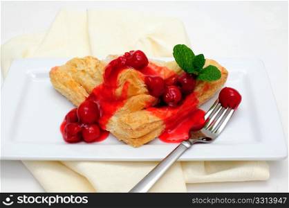 Turnover Topped With Cherries. Cherry Turnover with a topping of cherries and a red cherry sauce served on a white rectangular saucer and a light colored napkin
