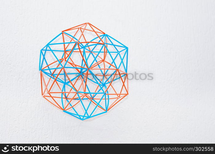 Turquoise and orange handmade three-dimensional model of geometric solid on a white textured background.. Bicolor Handmade Dimensional Model Of Geometric Solid