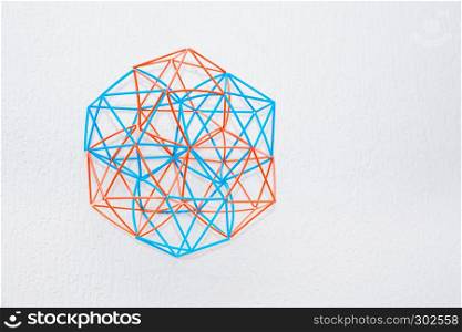 Turquoise and orange handmade three-dimensional model of geometric solid on a white textured background.. Bicolor Handmade Dimensional Model Of Geometric Solid