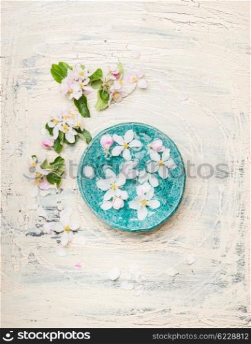 Turquoise blue water bowl with white blossom on light shabby chic wooden background, top view.