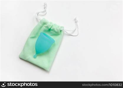 Turquoise menstrual cup on green small bag on white background. Concept zero waste, savings, minimalism, these days. Feminine hygiene product, flat lay, copy space. Horizontal.
