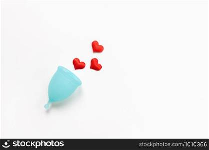 Turquoise menstrual cup on white background with red hearts. Concept zero waste, savings, minimalism, these days. Feminine hygiene product, flat lay, copy space. Horizontal.