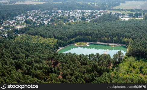 Turquoise rectangular lake in a forest landscape in front of a large camping site, remains of sand mining