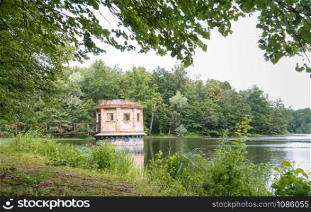 turret with a shutter on a forest pond, an old abandoned structure on a pond, vilgeiten pond, kolosovka village, Zelenograd city district, Kaliningrad region, Russia, August 18, 2019. an old abandoned structure on a pond, turret with a shutter on a forest pond