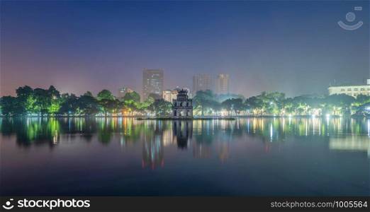 Turtle tower with modern skyscraper buildings and reflection in the middle of Hoan Kiem Lake in Downtown Hanoi. Urban city at night, Vietnam. Cityscape background.