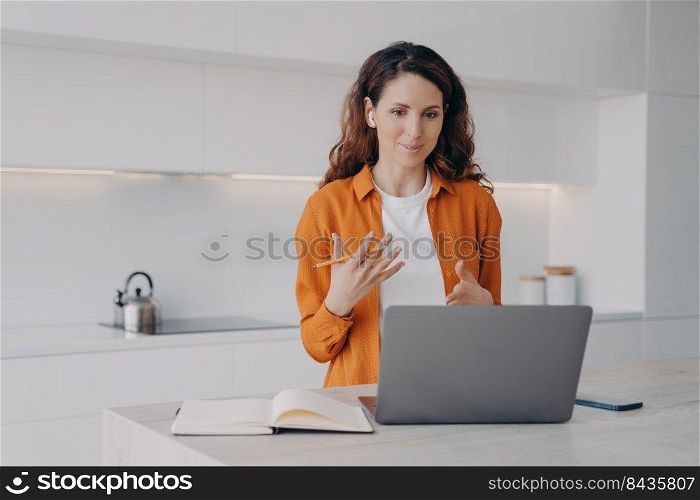 Tutor has lesson online on computer. Young pretty woman teaching students language online at her kitchen. Remote class and distance education at home on quarantine. Lecture via zoom.. Tutor has lesson online on computer. Young pretty woman teaching students language online.