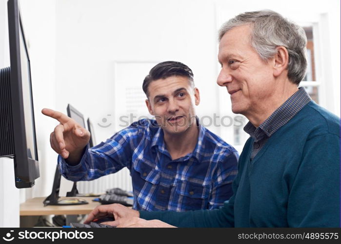 Tutor Helping Mature Man In Computer Class