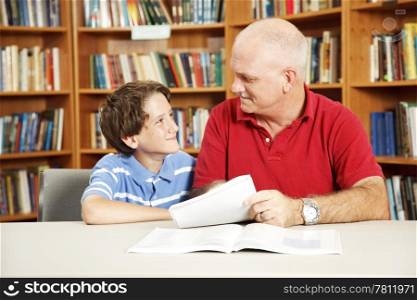Tutor or father helping a boy with his homework in the library.