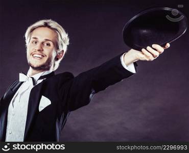 Tuxedo, male fashion, classical look concept. Elegantly dressed man throwing black fedora hat. Studio shot on dark background. Elegantly dressed man throwing black fedora hat
