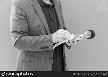 TV journalist or news reporter holding microphone and taking notes at press conference or media event