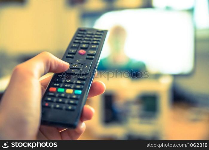 TV remote control in the foreground, tv in the blurry background.