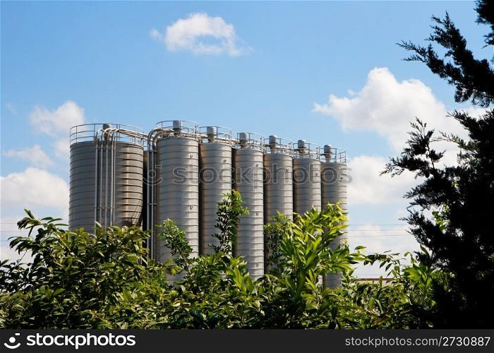 Twelve high metal tower silos on chemical plant behind the trees