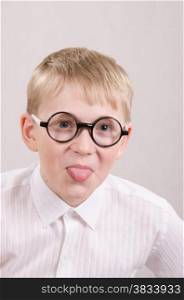 Twelve year old boy with glasses sitting on a chair and showing tongue in frame