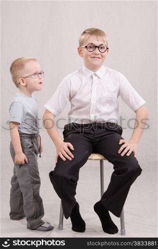 Twelve year old boy with glasses sitting on a chair, standing next to a year-old boy