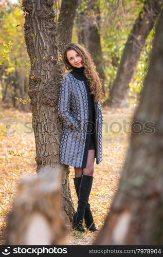 Twenty-five young beautiful girl walks by Europeans autumn forest. A young beautiful girl leaned back against the tree in the forest