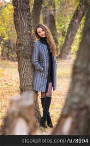 Twenty-five young beautiful girl walks by Europeans autumn forest. A young beautiful girl leaned back against the tree in the forest