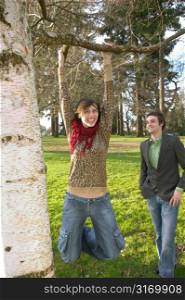 Twenty Something Girlfriend Hanging From A Branch In The Park And Laughing With Her Boyfriend