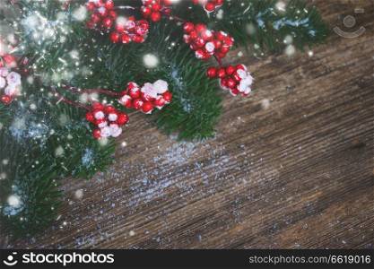 twig with red berries and green evergreen tree on aged wooden background with copy space, retro toned. red and white christmas