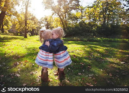 Twin girls wearing matching dresses face to face hugging and kissing