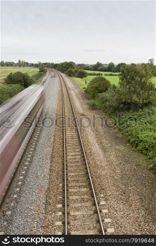 Twin railway tracks curving to the left, UK standard gauge, train moving away at speed (blurred).