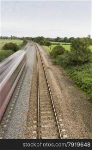 Twin railway tracks curving to the left, UK standard gauge, train moving away at speed (blurred).