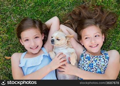 twin sisters playing with chihuahua dog lying on backyard lawn