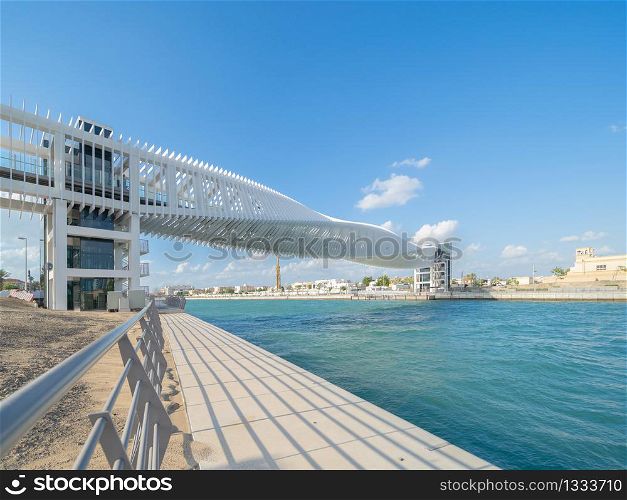 Twisted Bridge. Structure of architecture with lake or river, Dubai Downtown skyline, United Arab Emirates or UAE. Financial district and business area in urban city with blue sky background.