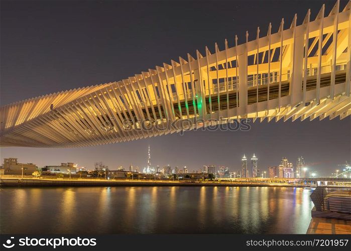 Twisted Bridge. Structure of architecture with lake or river, Dubai Downtown skyline, United Arab Emirates or UAE. Financial district and business area in urban city at night.