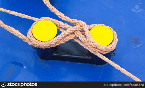 Twisted orange rope round a yellow bollard, large ship